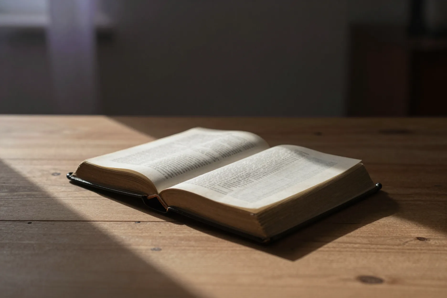 An open Bible on a plain wooden table in warm morning light.